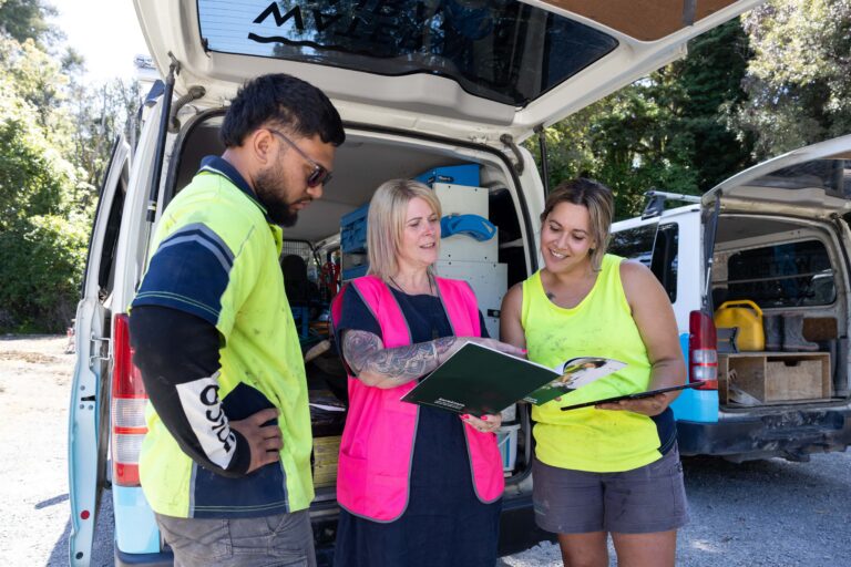 Apprentices and mentor reviewing paperwork beside a work van.