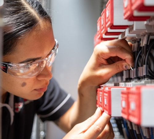 Apprentice electrician wearing safety glasses carefully wiring components inside an electrical panel.