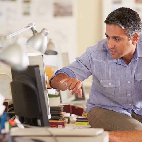 Professional in an office environment pointing at a computer screen during a discussion.